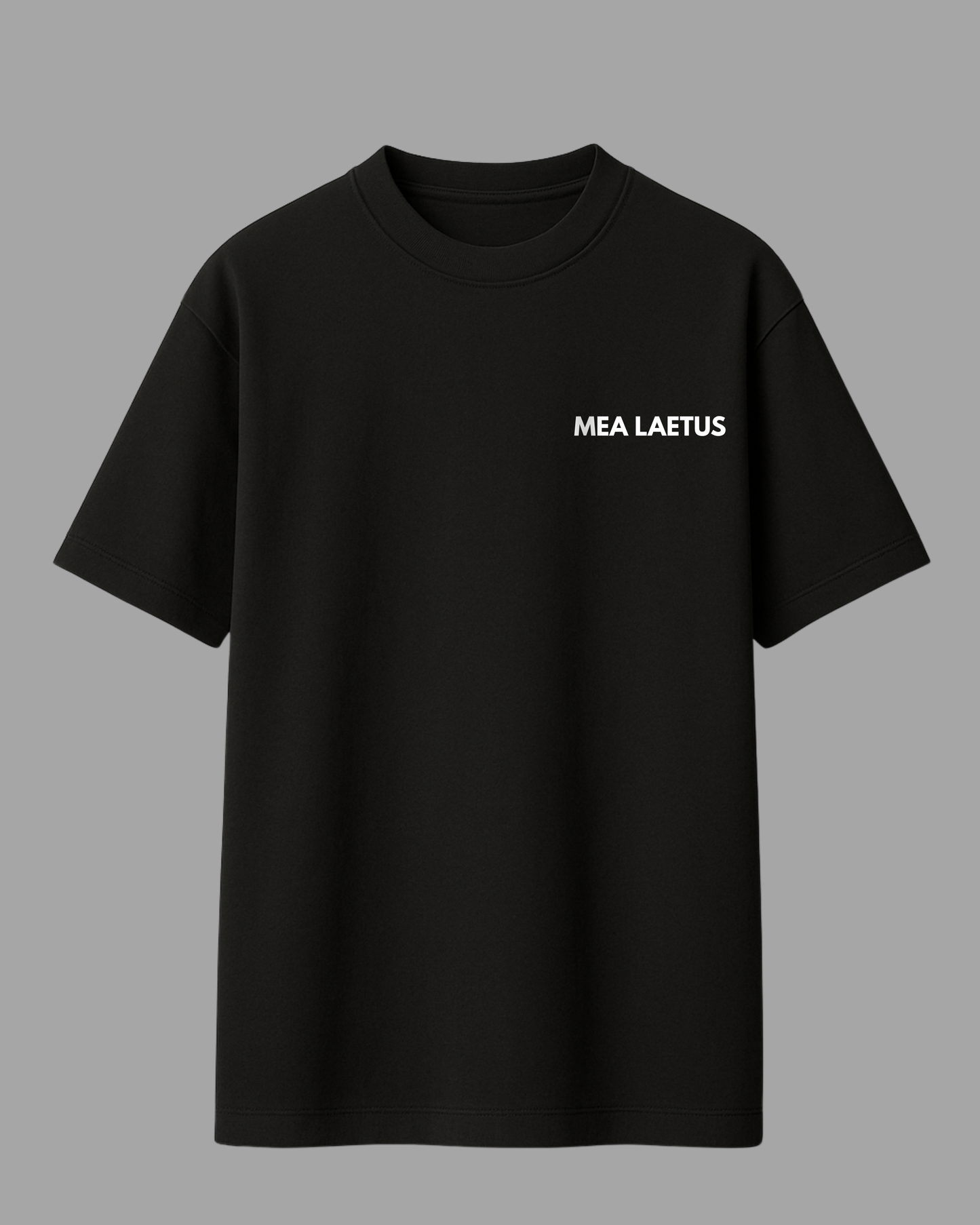 Schwarzes Oversized T-Shirt mit weißem MEA LAETUS Brustlogo auf grauem Hintergrund. T-Shirt Frontansicht Flatlay.