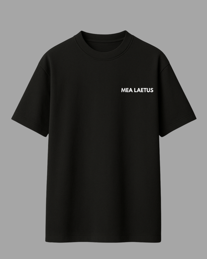 Schwarzes Oversized T-Shirt mit weißem MEA LAETUS Brustlogo auf grauem Hintergrund. T-Shirt Frontansicht Flatlay.