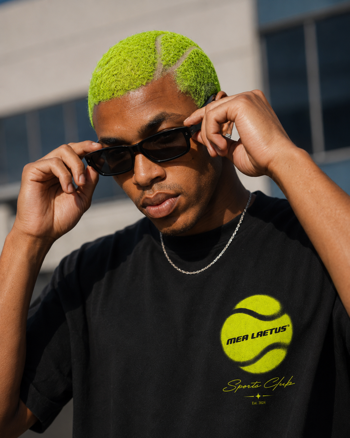 Porträt eines Models im schwarzen MEA LAETUS Tennis Club Shirt für Herren mit neongelbem Tennisball-Brustmotiv und schwarzer Sonnenbrille.