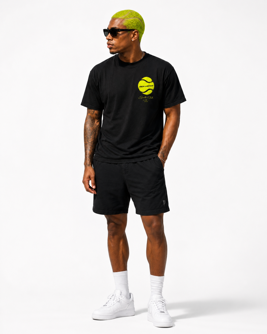 Ganzkörperansicht eines Models im schwarzen Tennis T-Shirt für Herren mit kleinem Neon-Frontprint, Shorts und weißen Sneakern.
